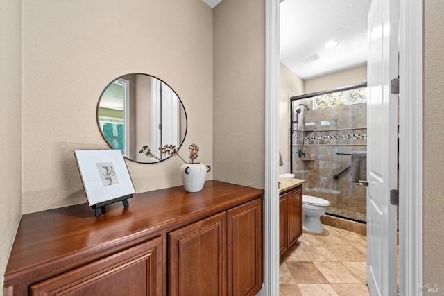 bathroom with vanity, a textured wall, a shower stall, and toilet