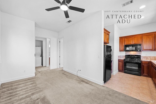 kitchen featuring ceiling fan, visible vents, stacked washing maching and dryer, light countertops, and black appliances