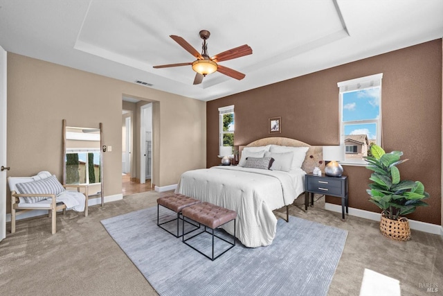carpeted bedroom featuring a tray ceiling, visible vents, and baseboards