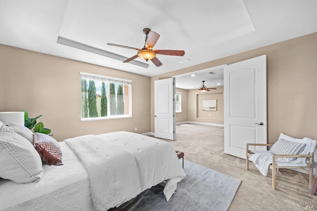 bedroom featuring a ceiling fan, baseboards, light carpet, and a tray ceiling