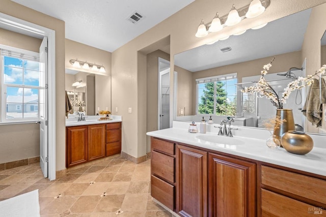 bathroom featuring baseboards, a sink, two vanities, and visible vents