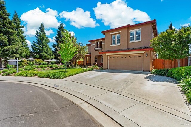 mediterranean / spanish-style house with a garage, fence, stucco siding, a tiled roof, and driveway