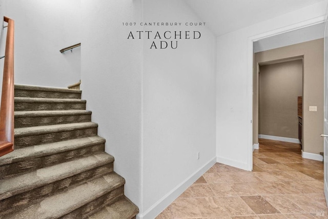 stairway featuring baseboards, stone finish flooring, and lofted ceiling