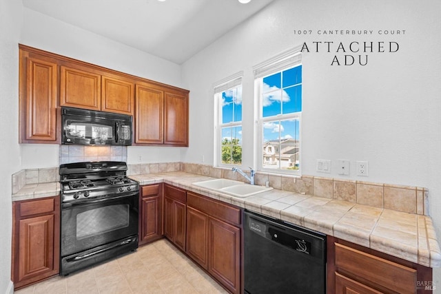 kitchen with a sink, brown cabinetry, black appliances, and tile countertops