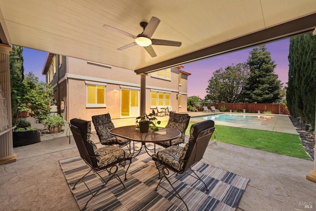 patio terrace at dusk with a fenced backyard, outdoor dining area, a fenced in pool, and ceiling fan