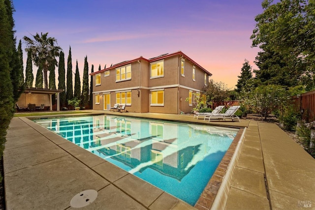 pool at dusk featuring a patio area, an outdoor pool, and fence
