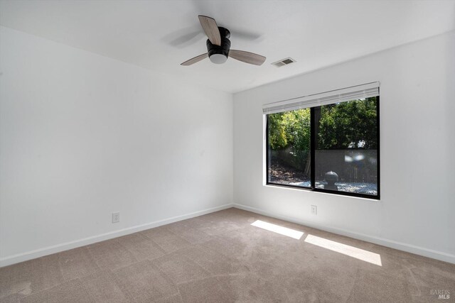 carpeted spare room featuring ceiling fan, visible vents, and baseboards