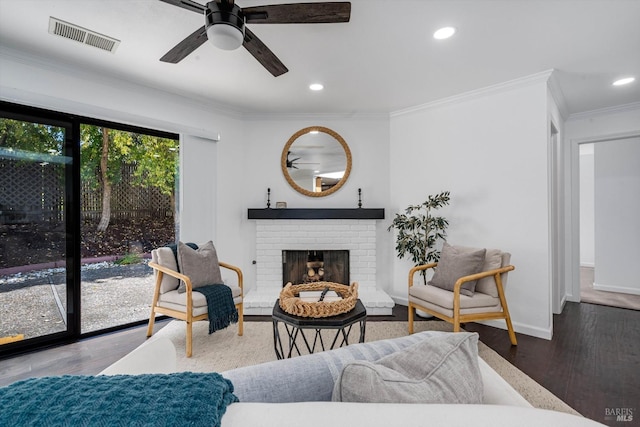 living area with a ceiling fan, visible vents, a brick fireplace, wood finished floors, and ornamental molding