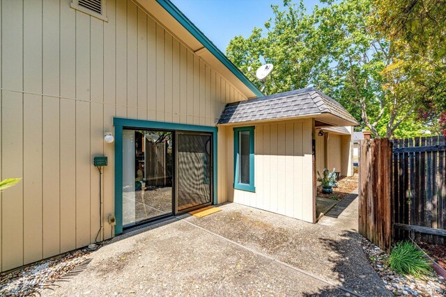 view of exterior entry with a patio, a shingled roof, and fence