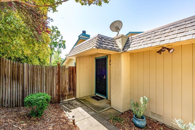 property entrance featuring roof with shingles, fence, visible vents, a chimney, and mansard roof