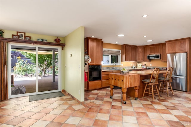 kitchen with a kitchen bar, appliances with stainless steel finishes, a sink, light countertops, and recessed lighting