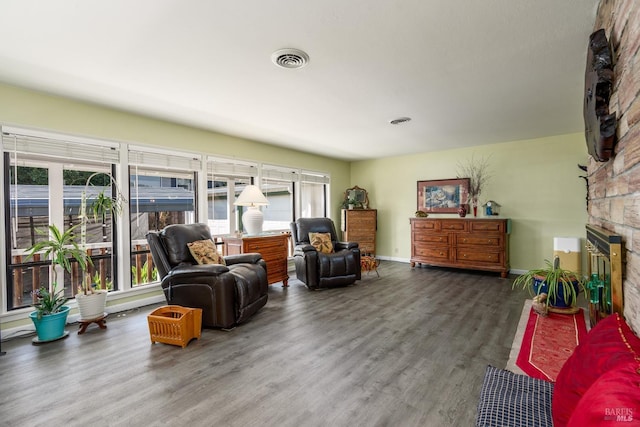 living area with baseboards, visible vents, a stone fireplace, and wood finished floors