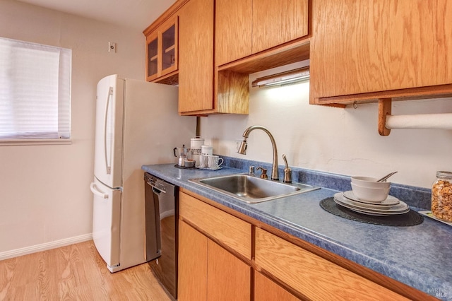 kitchen featuring dark countertops, a sink, light wood finished floors, dishwasher, and glass insert cabinets