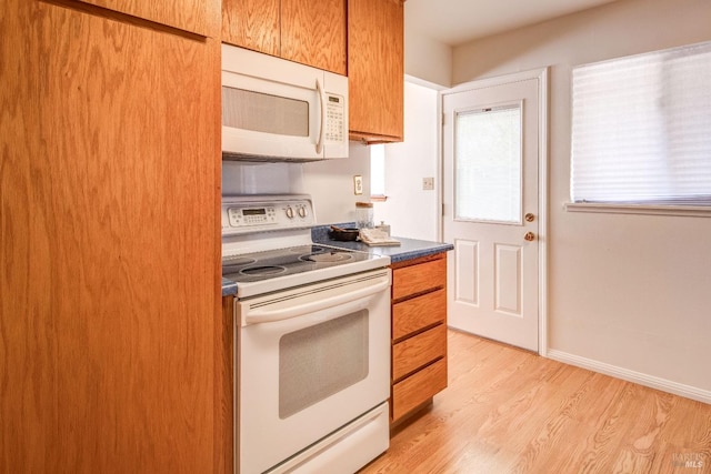 kitchen featuring brown cabinetry, dark countertops, light wood finished floors, and white appliances