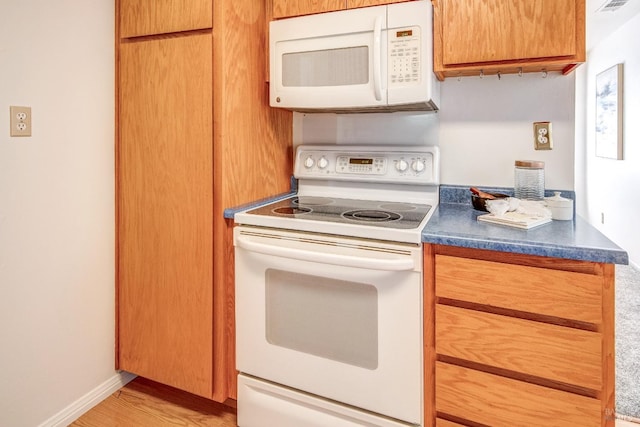 kitchen featuring dark countertops, brown cabinets, light wood finished floors, and white appliances