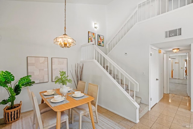 dining space with visible vents, baseboards, a chandelier, a high ceiling, and stairs