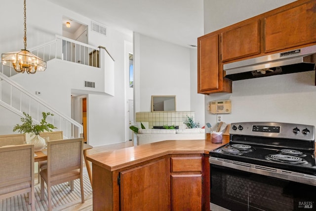 kitchen with brown cabinets, electric range, an inviting chandelier, under cabinet range hood, and visible vents