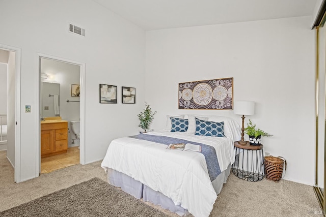 bedroom with visible vents, a towering ceiling, baseboards, ensuite bathroom, and light colored carpet