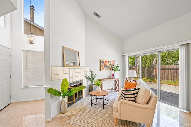 living area featuring a tiled fireplace, high vaulted ceiling, baseboards, and visible vents