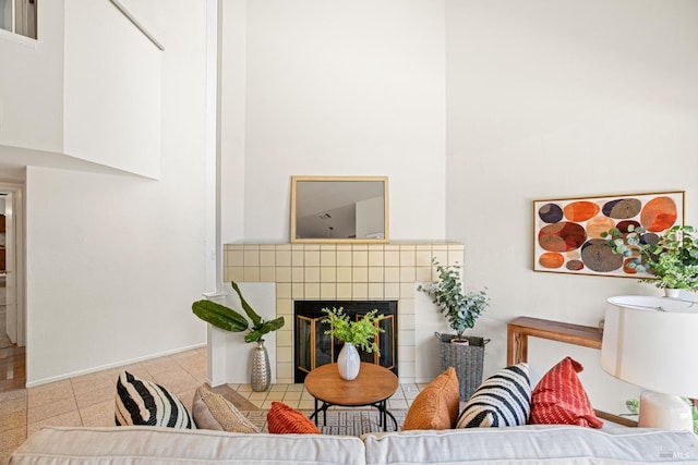 living area featuring a tiled fireplace, baseboards, and a high ceiling