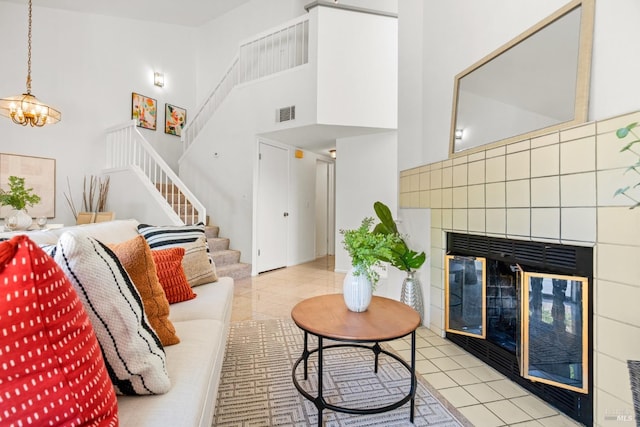 living area featuring stairs, a towering ceiling, a tile fireplace, light tile patterned floors, and a notable chandelier