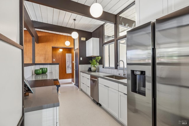 kitchen with a sink, stainless steel appliances, backsplash, beamed ceiling, and white cabinetry