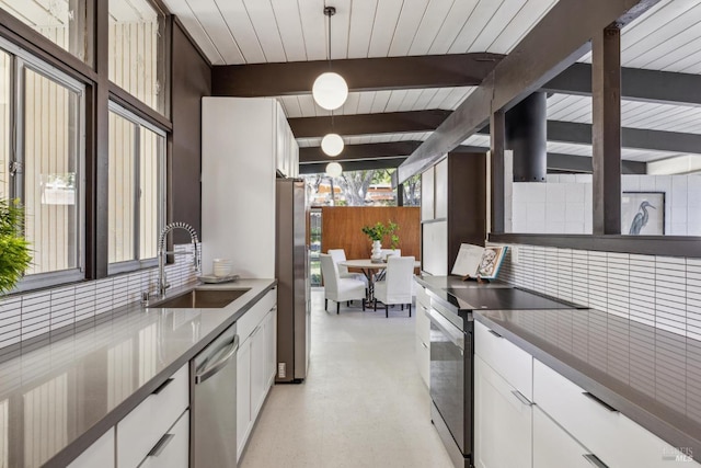 kitchen with appliances with stainless steel finishes, a sink, beam ceiling, white cabinets, and hanging light fixtures
