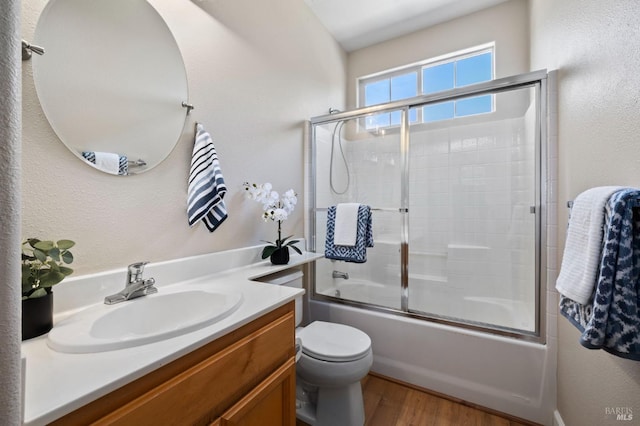 bathroom featuring vanity, a textured wall, wood finished floors, toilet, and combined bath / shower with glass door