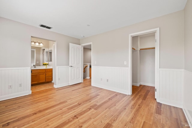 unfurnished bedroom featuring visible vents, a walk in closet, light wood-type flooring, a wainscoted wall, and a sink