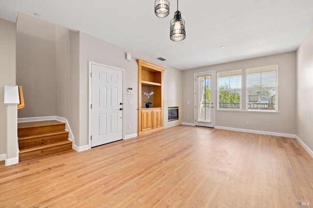 unfurnished living room featuring light wood-style floors, baseboards, stairs, and visible vents