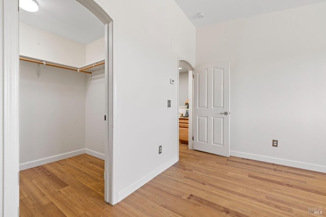 unfurnished bedroom featuring light wood-style floors, arched walkways, baseboards, and a closet