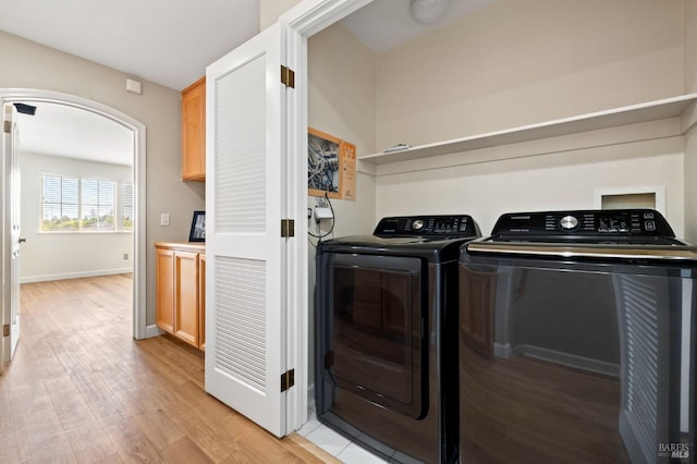 washroom featuring laundry area, washing machine and clothes dryer, arched walkways, baseboards, and light wood-style floors