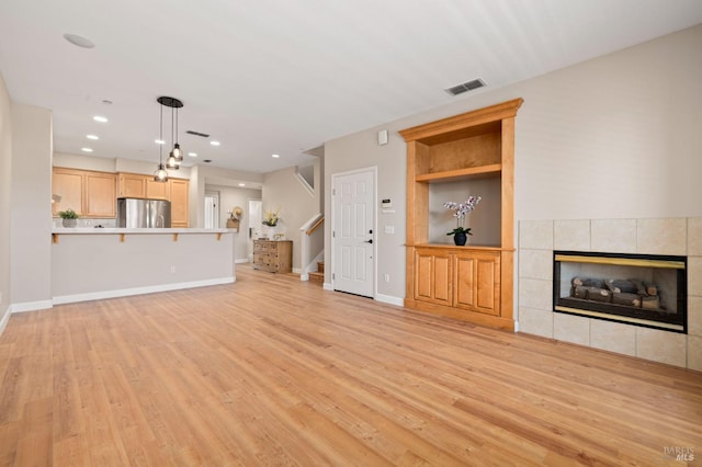 unfurnished living room with visible vents, a fireplace, baseboards, light wood-style floors, and stairs