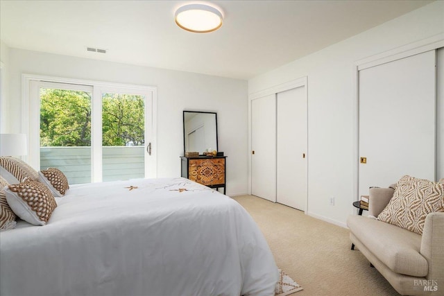 bedroom featuring multiple closets, visible vents, light carpet, and baseboards