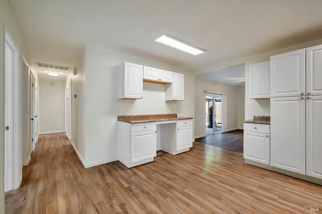 kitchen with built in study area, white cabinets, light wood-type flooring, and visible vents