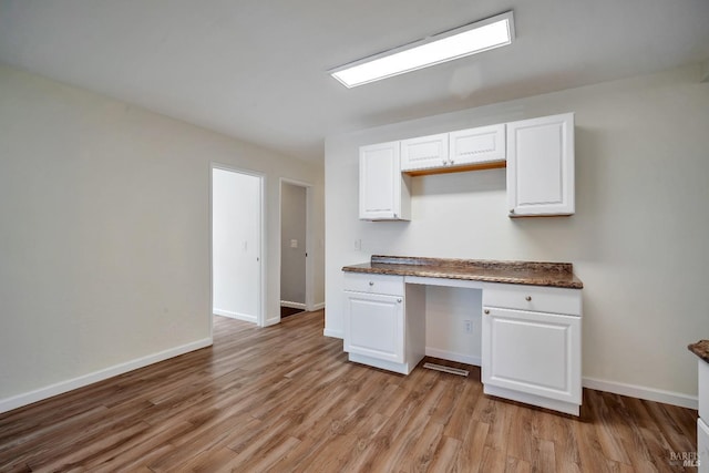 kitchen featuring white cabinets, dark countertops, built in desk, and light wood-type flooring
