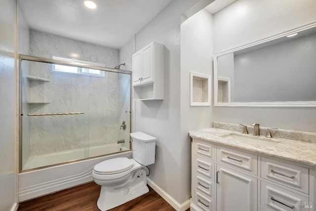 full bath with wood finished floors, vanity, baseboards, toilet, and shower / bath combination with glass door