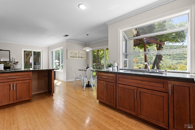 kitchen with brown cabinetry, visible vents, hanging light fixtures, a sink, and light wood-style floors