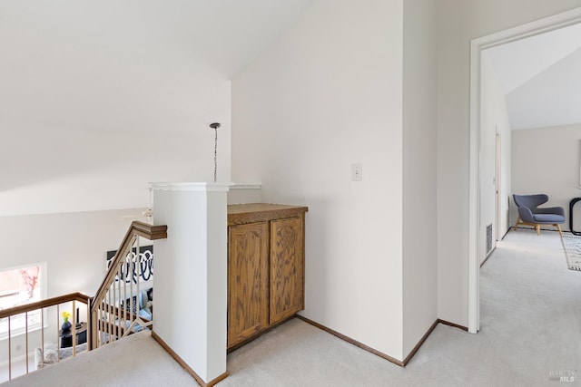 hall featuring light colored carpet, baseboards, vaulted ceiling, and an upstairs landing