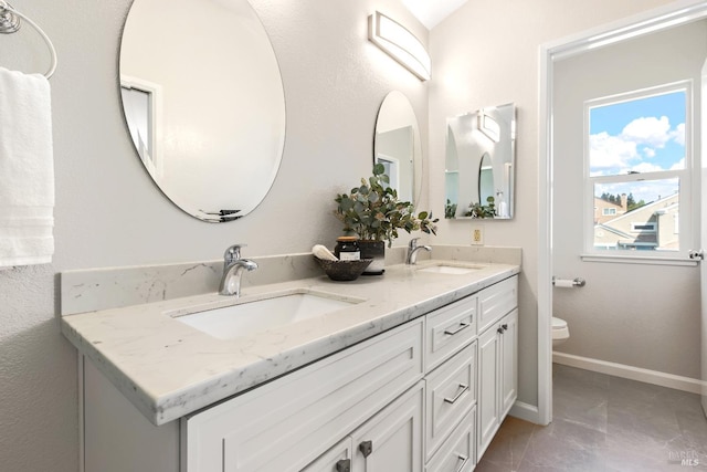 bathroom with baseboards, double vanity, toilet, and a sink
