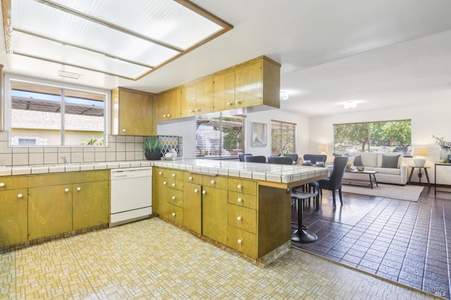 kitchen featuring decorative backsplash, a peninsula, white dishwasher, open floor plan, and tile countertops