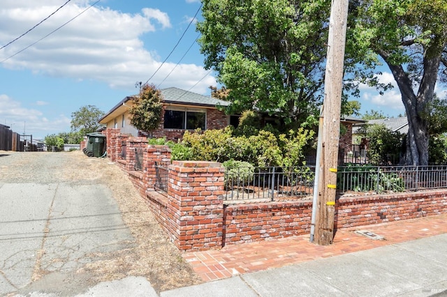 view of property hidden behind natural elements featuring brick siding, fence, and aphalt driveway