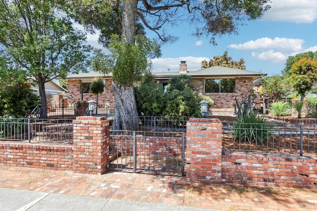 view of front of home with brick siding, a gate, a fenced front yard, and a chimney