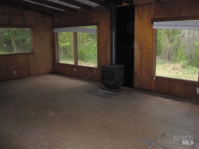 2750 Summerfield Rd, Santa Rosa, CA 95405 - unfurnished living room with beamed ceiling, wood walls, a healthy amount of sunlight, and a wood stove