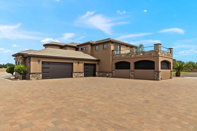 view of front facade featuring an attached garage, stone siding, stucco siding, decorative driveway, and a balcony