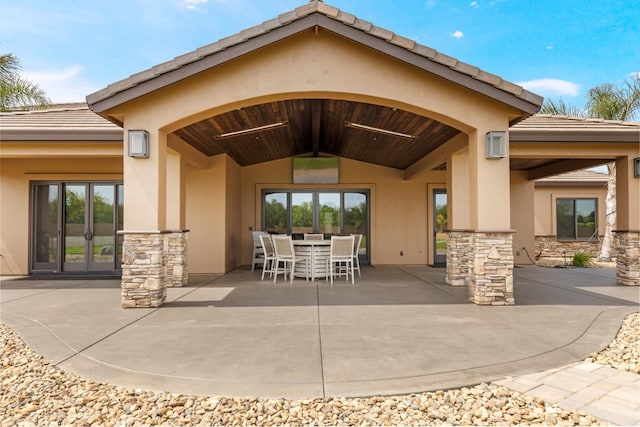 rear view of house with stone siding, stucco siding, a patio area, a tiled roof, and outdoor dining space