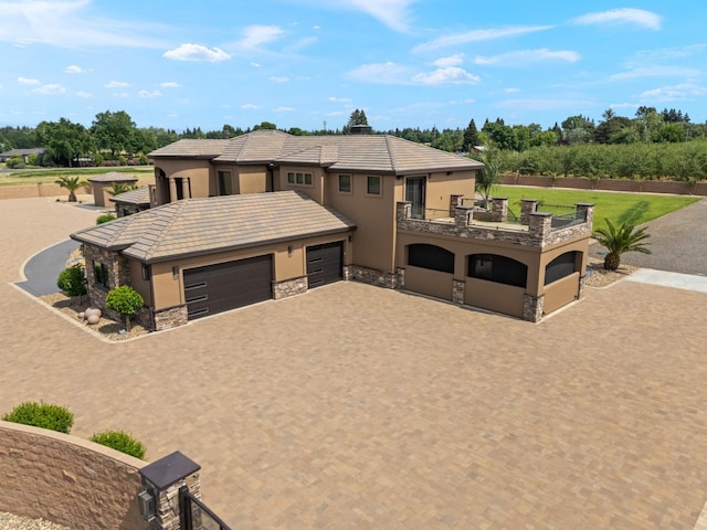 view of front facade with a garage, decorative driveway, a balcony, stone siding, and stucco siding