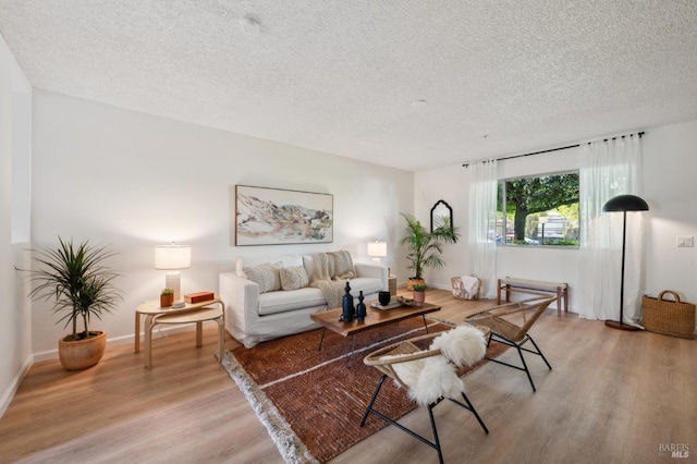 living area featuring light wood-type flooring, a textured ceiling, and baseboards