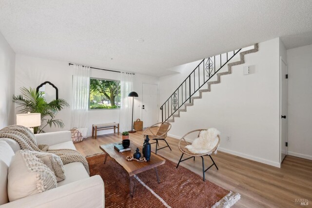 living room with stairs, a textured ceiling, baseboards, and wood finished floors