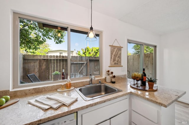 kitchen featuring plenty of natural light, a sink, white cabinetry, and hanging light fixtures
